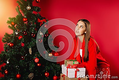 The girl is holding heavy gift boxes at home by the decorated tree Stock Photo