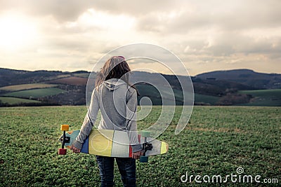 Girl holding longboard and walking across green field Stock Photo