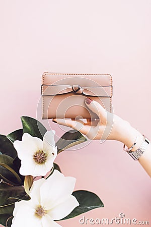 Girl holding a pink wallet on a gentle pastel background with a flower. Stock Photo