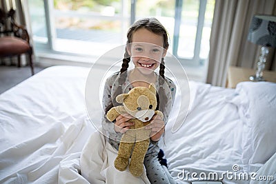 Girl holding teddy bear on bed in bedroom Stock Photo