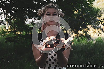 Girl holds a burning book in her hands. A young woman in a forest burns a book Stock Photo