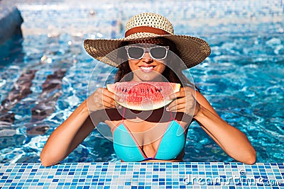 A girl holds half a red watermelon over a blue pool, relaxing o Stock Photo