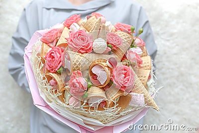 Girl holds in her hands an original bouquet consisting of pink flowers of a rose and various sweets Stock Photo