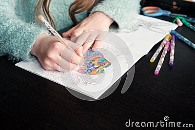 A girl holds a pencil in her hands and paints a coloring book. Colored pencils lie on the table. The development of creativity. Stock Photo