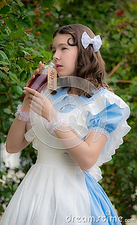 Girl in image of fairy tale heroine drinks drink of glass bottle Stock Photo