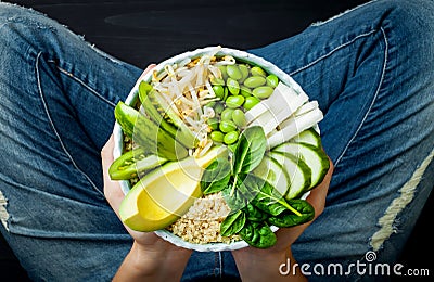 Girl in jeans holding vegan, detox green Buddha bowl with quinoa, avocado, cucumber, spinach, tomatoes, mung bean sprouts, edamame Stock Photo