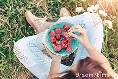 Girl in jeans sitting in summer grass and holding a plate of strawberries Stock Photo