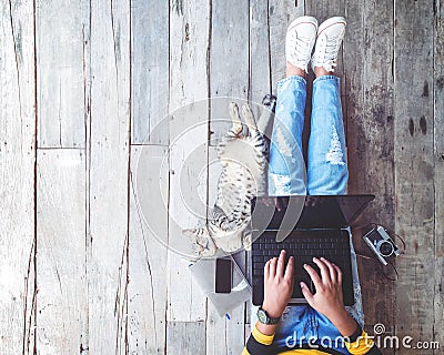 Girl in jeans working on the laptop computer assisted by her cat on the wooden floor Stock Photo