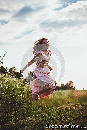 girl jumping in the field in a pink dress Stock Photo