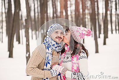 Girl kissing her boyfriend on the cheek in winter outdoors. Wearing cozy warm clothes, knitted hat and gloves . Winter dating con Stock Photo