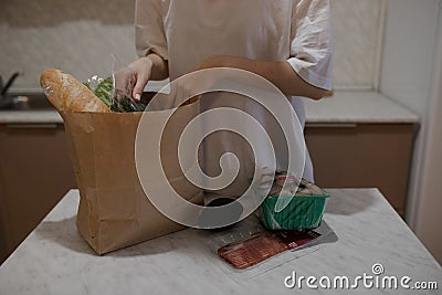 The girl lays out the products from the bag on the table. A close-up of the girl pulls groceries out of a paper bag Stock Photo