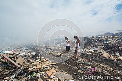 Girl leading her friend through the smoke at garbage dump Stock Photo