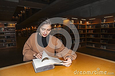 Girl in library turns page of book with smile Stock Photo