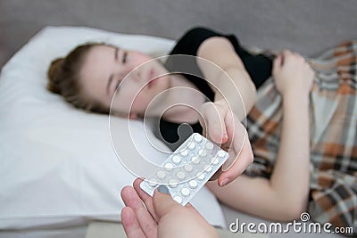 The girl lies in bed, is sick and takes pills from her hands for treatment. Pain during menstruation in a teenage girl Stock Photo