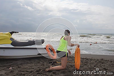 Girl lifeguard on duty keeping a buoy at the beach. Water scooter, lifeguard rescue equipment orange preserver tool on beach. Saf Stock Photo