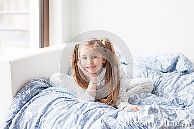 A girl in light gray pajamas sits on a bed by the window, the child woke up in the morning, morning yoga Stock Photo