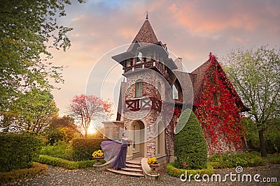 A girl in a lilac dress standing at the door of a beautiful art Nouveau cottage in the autumn garden Stock Photo