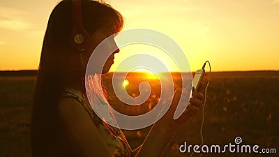 Girl listening to music and dancing in the rays of a beautiful sunset. a young girl in headphones and with a smartphone Stock Photo