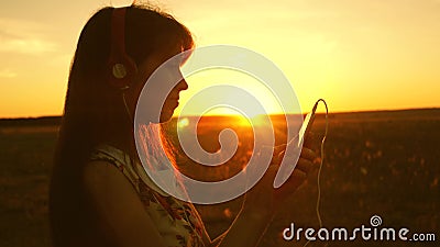 Girl listening to music and dancing in the rays of a beautiful sunset. a young girl in headphones and with a smartphone Stock Photo