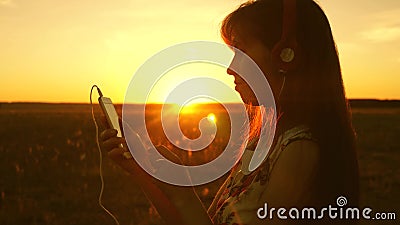Girl listening to music and dancing in the rays of a beautiful sunset. a young girl in headphones and with a smartphone Stock Photo