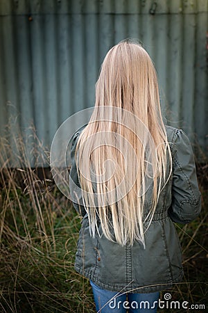 Girl with long blonde hair from behind by a rusty green wall Stock Photo