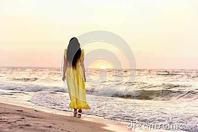 A girl in a long dress with long black hair walks at dawn along a deserted beach along Stock Photo