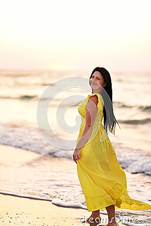 A girl in a long dress with long black hair walks at dawn along a deserted beach Stock Photo