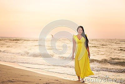 A girl in a long dress with long black hair walks at dawn along a deserted beach Stock Photo