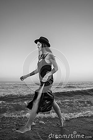 girl in long dress and hat enters thoughtfully into raging sea Stock Photo