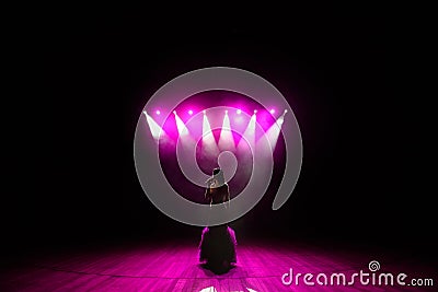 Girl in long gown performing on stage. Girl singing on the stage in front of the lights. Silhouette of singer standing Stock Photo