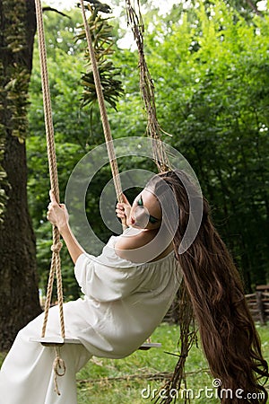 Girl with long hair in white dress is riding rope swing in fores Stock Photo