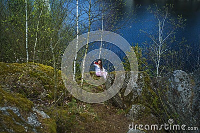 A girl sits in a park near a recreation area in nature. A girl looks from a height at the river.A young girl stands near a cliff, Stock Photo