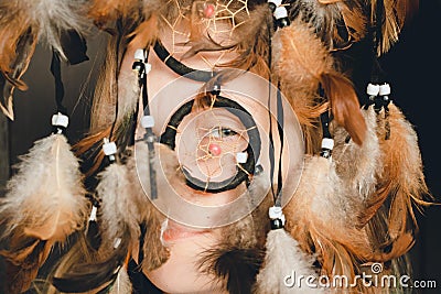 The girl looks through the ring of the dream catcher with one eye, feathers caress her tender face. Stock Photo