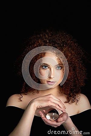 A girl with lush curly red hair. Holds in his hands a glass globe. Mystery,a premonition of the future. Stock Photo