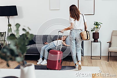 Girl lying on the couch, her mother standing with a suitcase. Travel, lodging Stock Photo