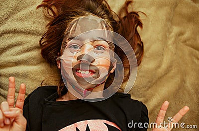 Girl made a face mask. Girl 9 years old or 10 years old. Facial care in joy. The girl made a cellulose mask Stock Photo