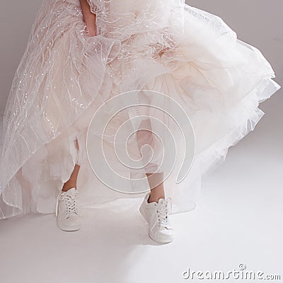 The girl in magnificent wedding dress and white sneakers, legs close-up. Runaway bride Stock Photo