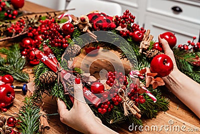 Girl making Christmas door wreath using natural fir branches, red colorful berries, wooden toys, cones and cinnamon sticks. Stock Photo