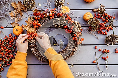 Girl making floral autumn door wreath using colorful rosehip berries, rowan, dry flowers and pumpkin Stock Photo