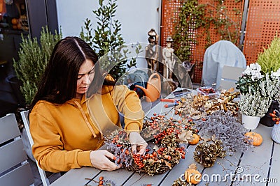 Girl making floral autumn door wreath using colorful rosehip berries, rowan, dry flowers and pumpkins Stock Photo