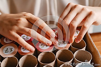 Girl making handmade advent calendar house from toilet paper rolls and carton box, close up. Stock Photo