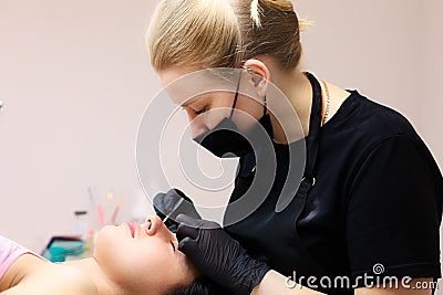 Girl of the master of lamination of cilia sits at the head of the client and performs the procedure Stock Photo