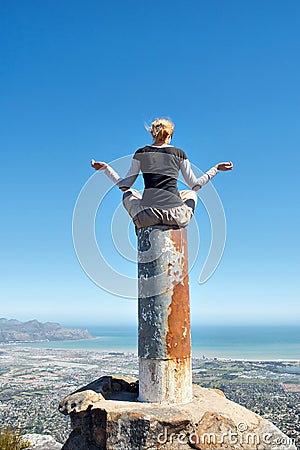 Girl meditates on top of column in mountains Stock Photo