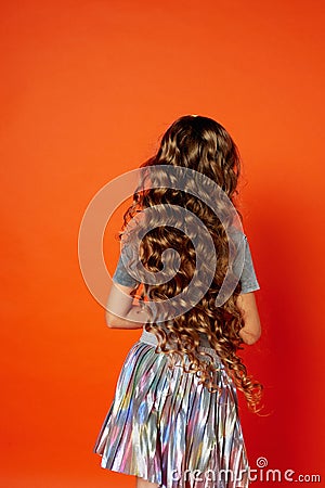 Girl on orange background in the Studio. Very long curly hair like in a fairy tale.Rapunzel Stock Photo