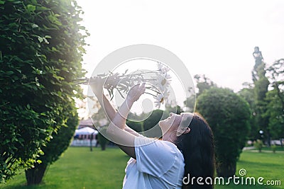 A girl in the park near a large bush sniffs a bouquet of daisies. Good luck, happy pastime, good mood. The concept of healthy Stock Photo