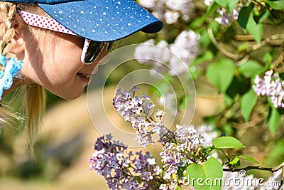 A girl in the park smells lilac flowers on a tree. Allergy to pollen Stock Photo