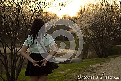 Girl in park at sunset making heart shape with hands behind back Stock Photo