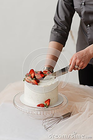 pastry chef cuts white strawberry cake with cream with a knife Stock Photo