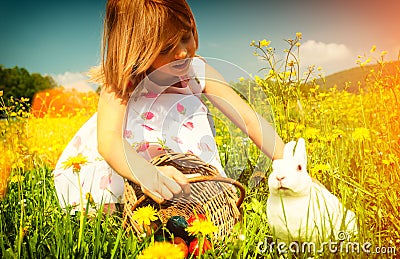 Girl petting Easter bunny on meadow with eggs Stock Photo