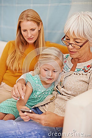 Girl, phone and social media at a home with grandmother, family and mother together with game. Learning, online and Stock Photo